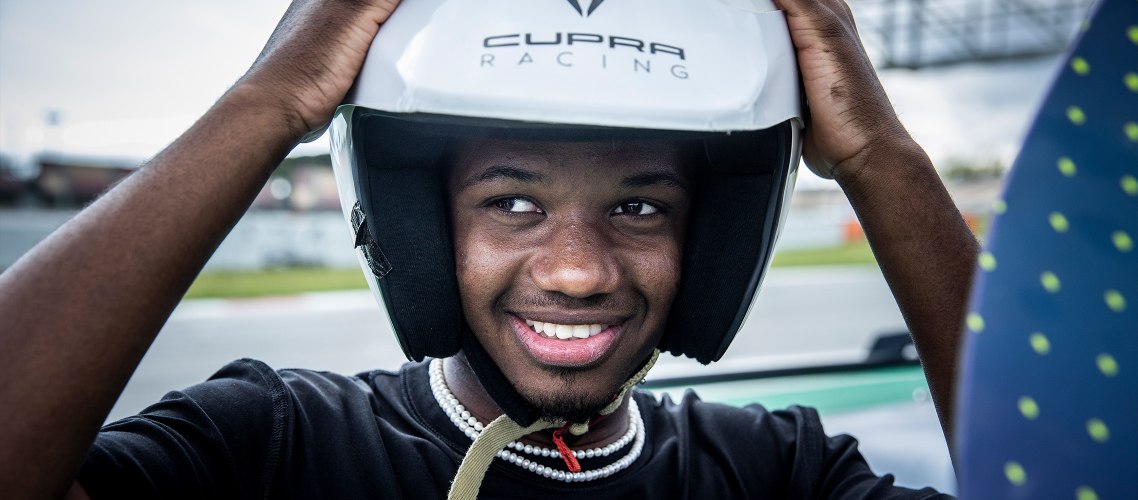 Ein kleiner Junge setzt sich den weißen CUPRA Rennfahrer Helm auf.