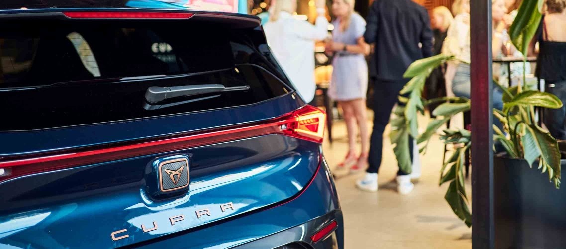 nnenansicht der CUPRA City Garage während der 'Spanish Design Night' mit Gästen, die die ausgestellten Designs bewundern. Im Vordergrund steht der CUPRA Born.