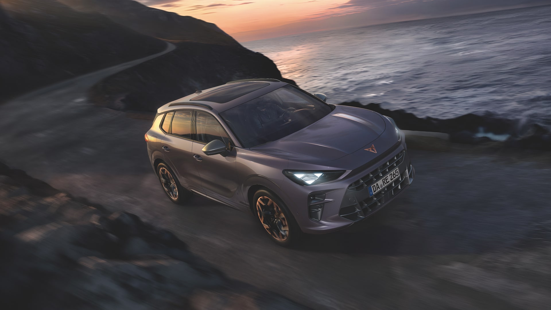 Ein CUPRA Terramar Elektrofahrzeuge fährt über eine Landstraße, im Hintergrund sieht man das Meer.