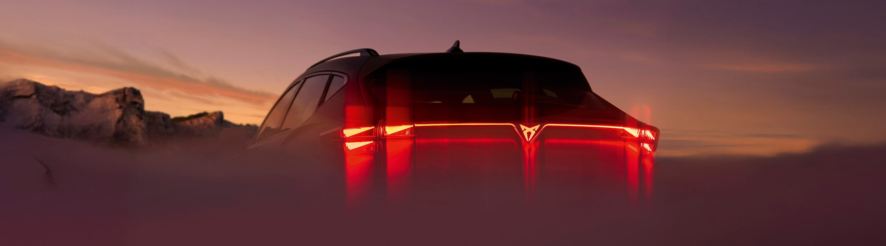 CUPRA Frühlingsangebote, Rückansicht eines CUPRA Fahrzeugs mit den roten Rückleuchten. Im Hintergrund ist eine Berglandschaft und ein Sonnenuntergang zu erkennen.