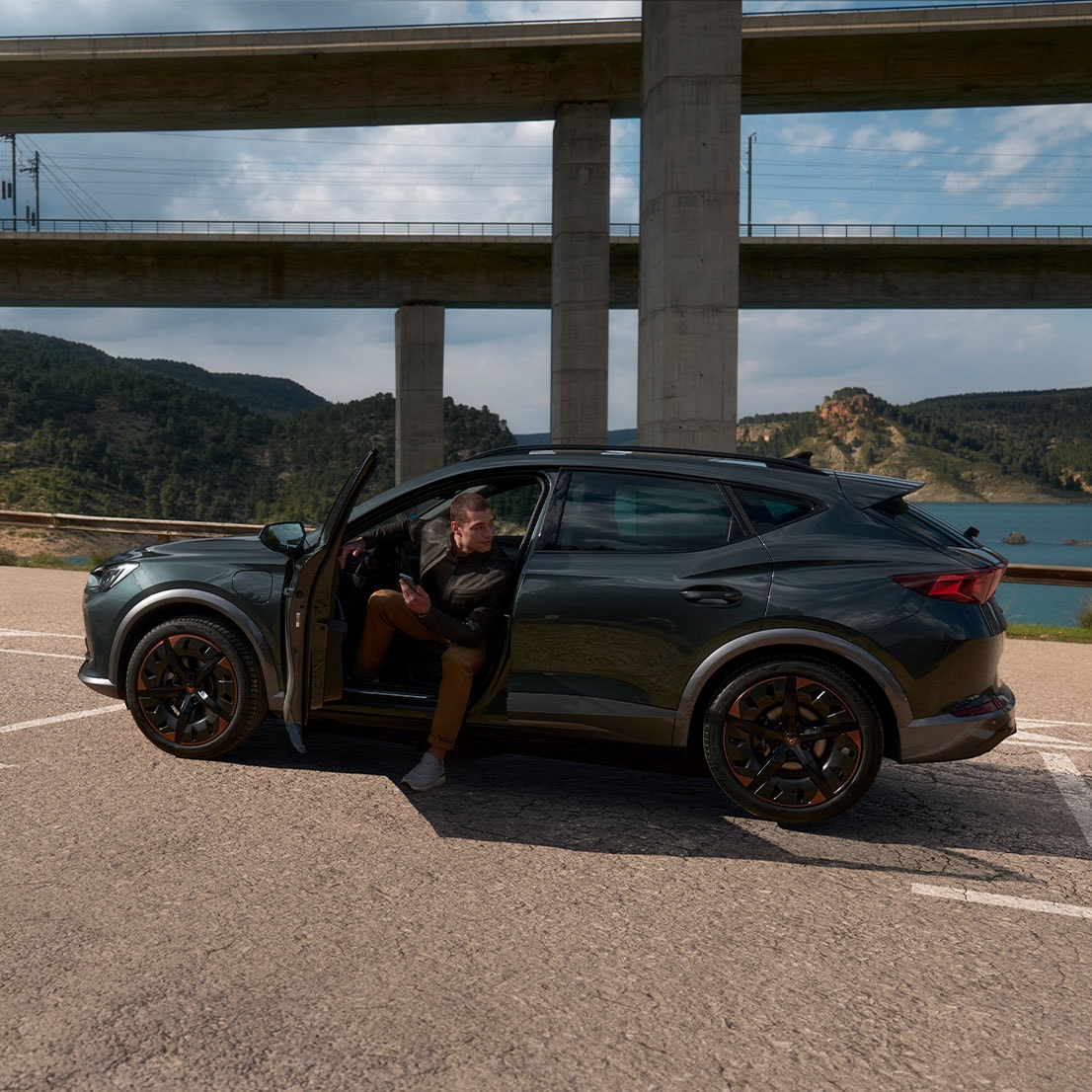 Mann steigt aus CUPRA Formentor aus und schaut nach rechts, im Hintergrund Autobahnbrücken und begrünte Berge