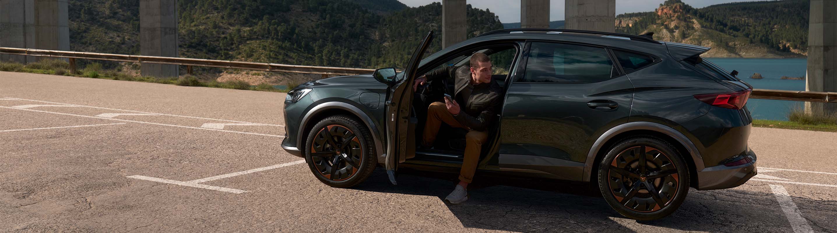 Mann steigt aus CUPRA Formentor aus und schaut nach rechts, im Hintergrund Autobahnbrücken und begrünte Berge