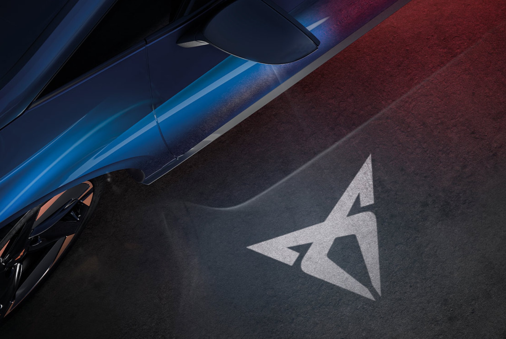 Vogelperspektive eines blauen CUPRA Born, der das Welcome Light aktiviert hat und das CUPRA Logo auf den grauen Betonboden projiziert wird. 