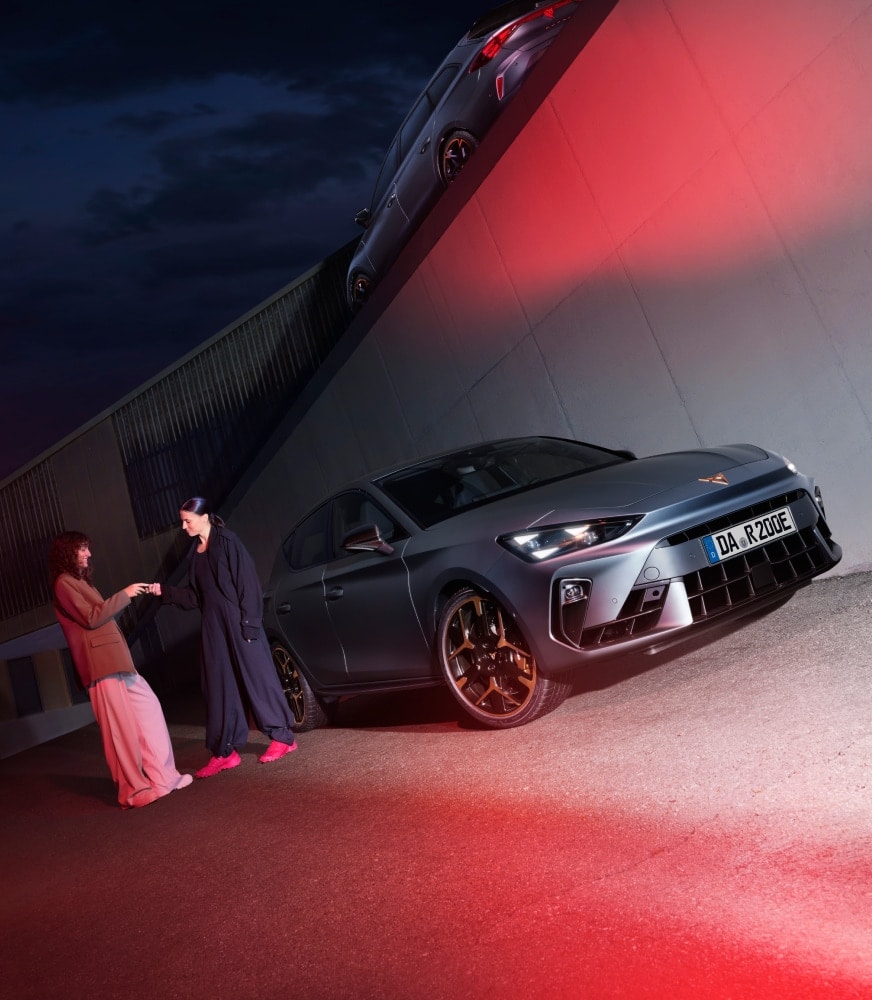 Zwei Frauen bei Nacht vor dem CUPRA Leon e-HYBRID – ikonisches Lichtdesign, mutige Linien und urbane Haltung in einer außergewöhnlichen Kulisse.