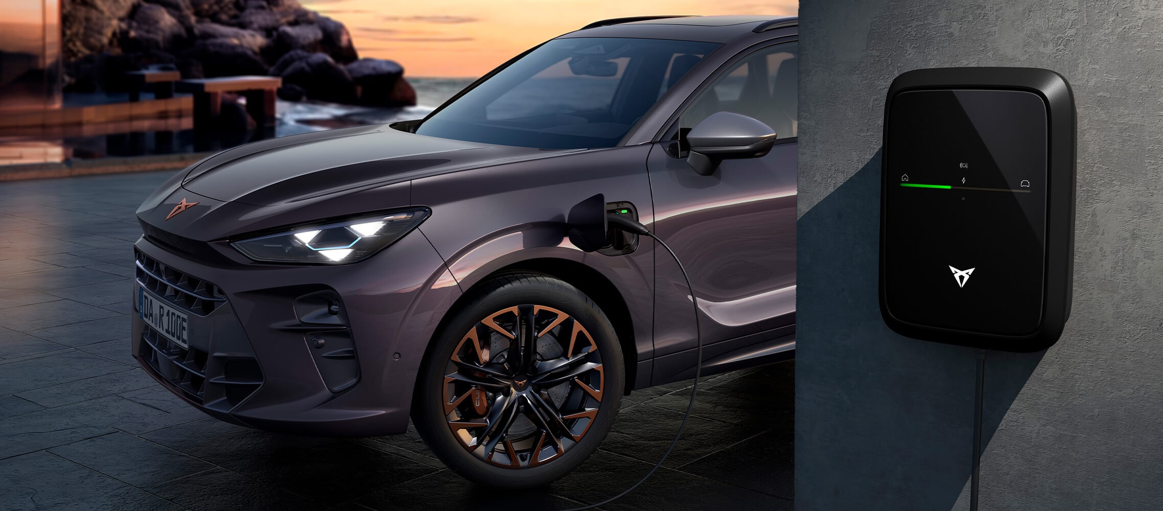 CUPRA Terramar VZ PHEV Firmenwagen für CUPRA Fleet Solutions in der Farbe „Dark Void“, geparkt während des Ladevorgangs mit dem CUPRA-Ladegerät vor einer malerischen Kulisse bei Sonnenuntergang.