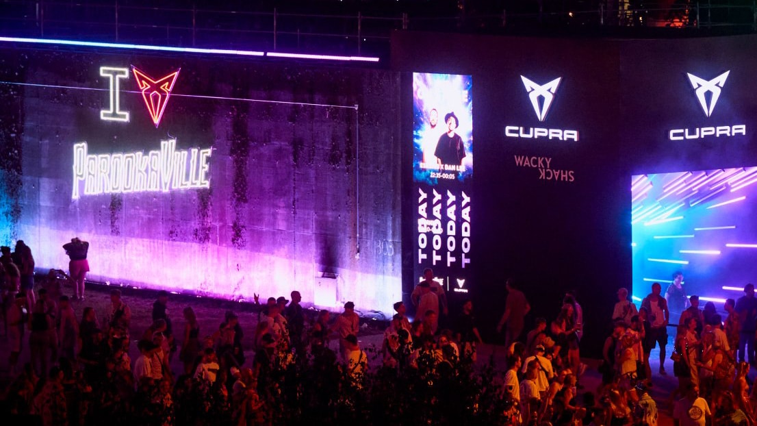 Die Konzertbühne ist in orangefarbenes Licht getaucht und links, rechts und in der Mitte mit dem CUPRA Logo auf Bildschirmen versehen. Die Konzertbühne ist in orangefarbenes Licht getaucht und links, rechts und in der Mitte mit dem CUPRA Logo auf Bildschirmen versehen.