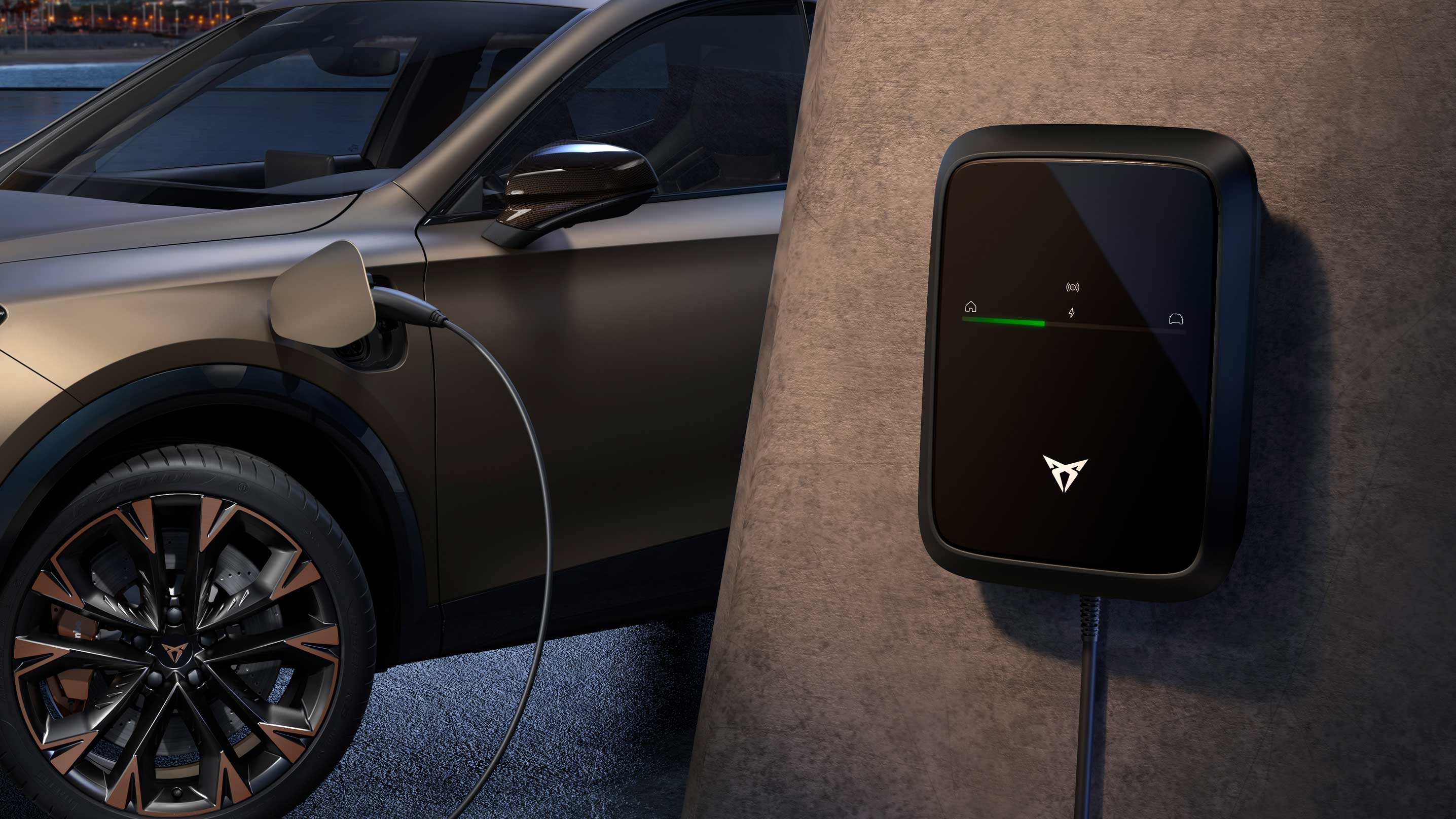 Ein CUPRA Formentor e-Hybrid wird an eine an der Wand montierte CUPRA-Wallbox zum Aufladen angeschlossen. Das Fahrzeug hat markante bronzefarbene Felgen und befindet sich in einer modernen Umgebung. Die Wallbox zeigt eine grüne Statusleuchte an, die den Ladevorgang signalisiert.