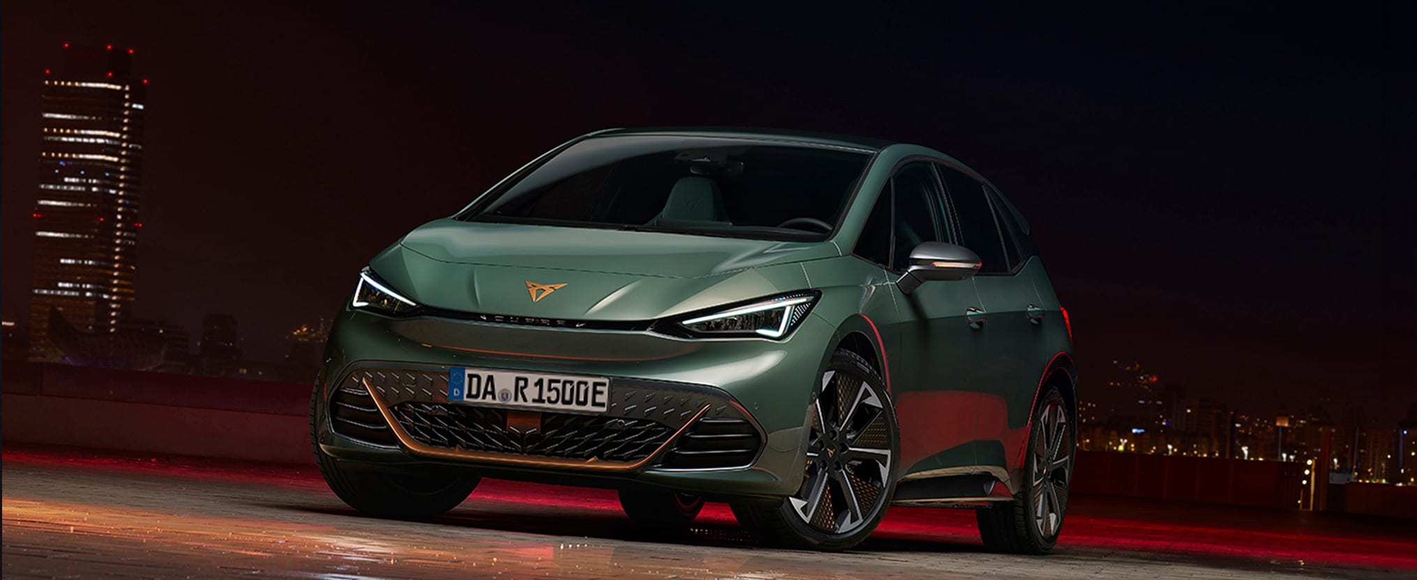 CUPRA Born Elektrofahrzeug in grün, angetrieben durch einen Elektromotor steht vor einer Skyline in Abendstimmung.