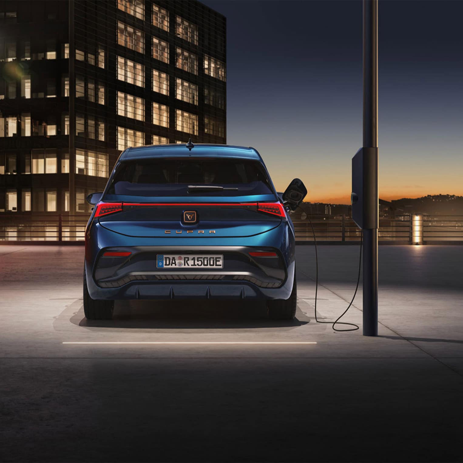 CUPRA Born, der an einer öffentlichen Ladestation angeschlossen ist, in minimaler und industrieller Umgebung.