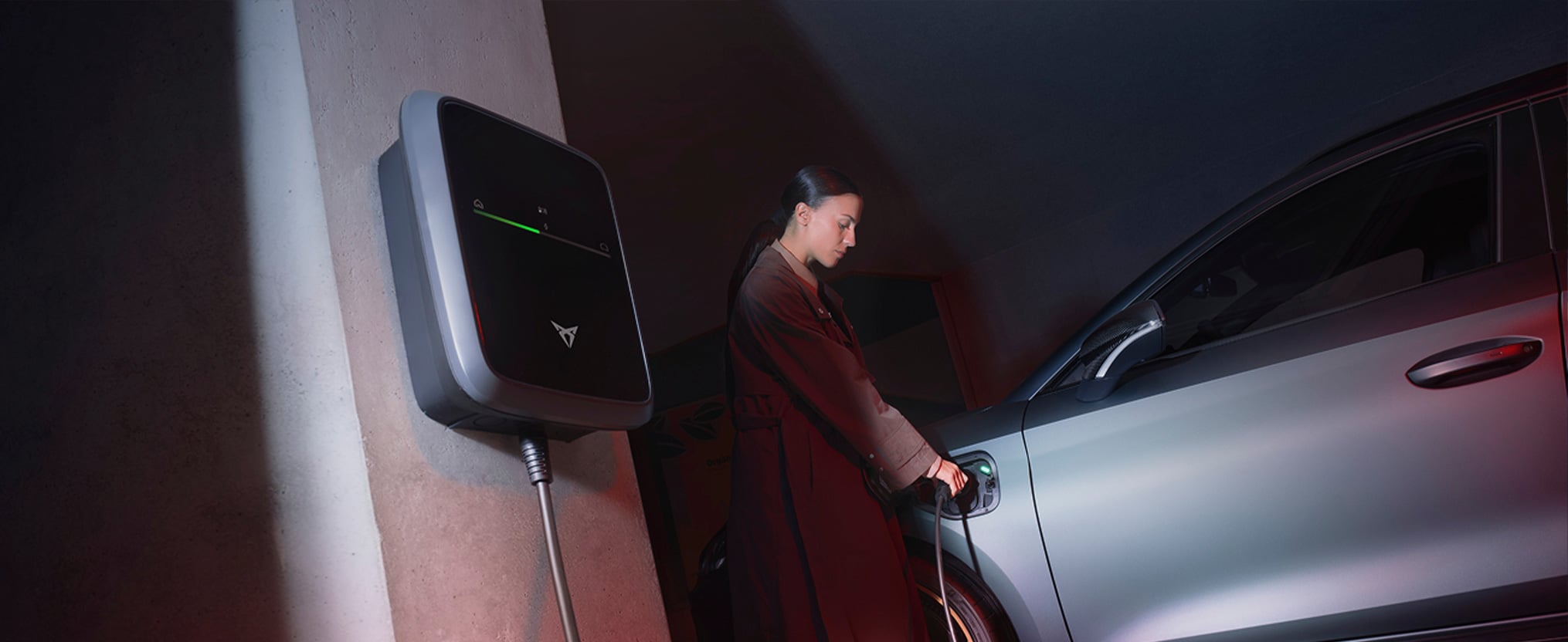 CUPRA e-HYBRID steht neben einer Wallbox und wird von einer Frau geladen.