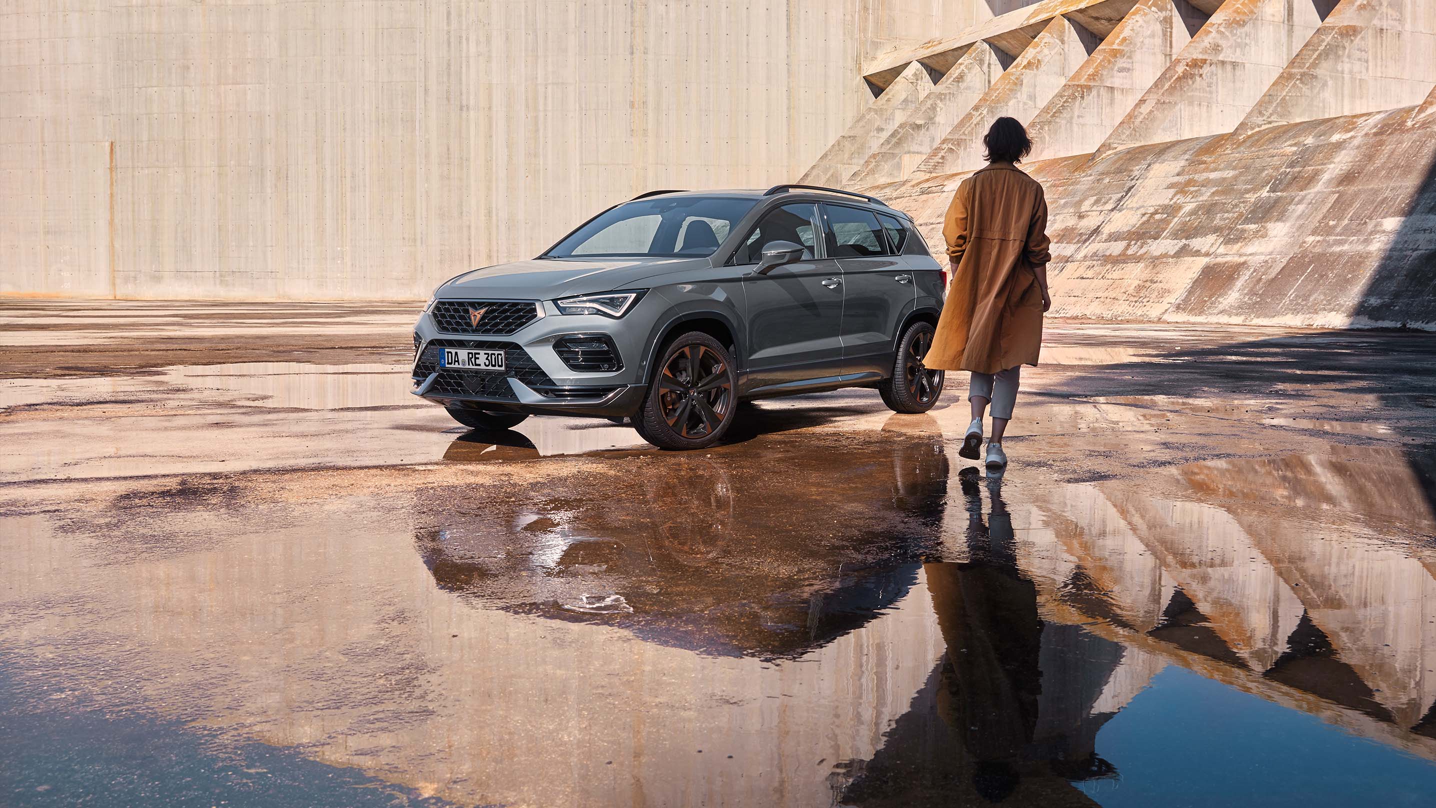 Eine Person geht auf den CUPRA Ateca zu und zeigt dabei die markanten, athletischen Linien und die dynamische Form des Fahrzeugs, die den Spirit des CUPRA Tribes verkörpern.