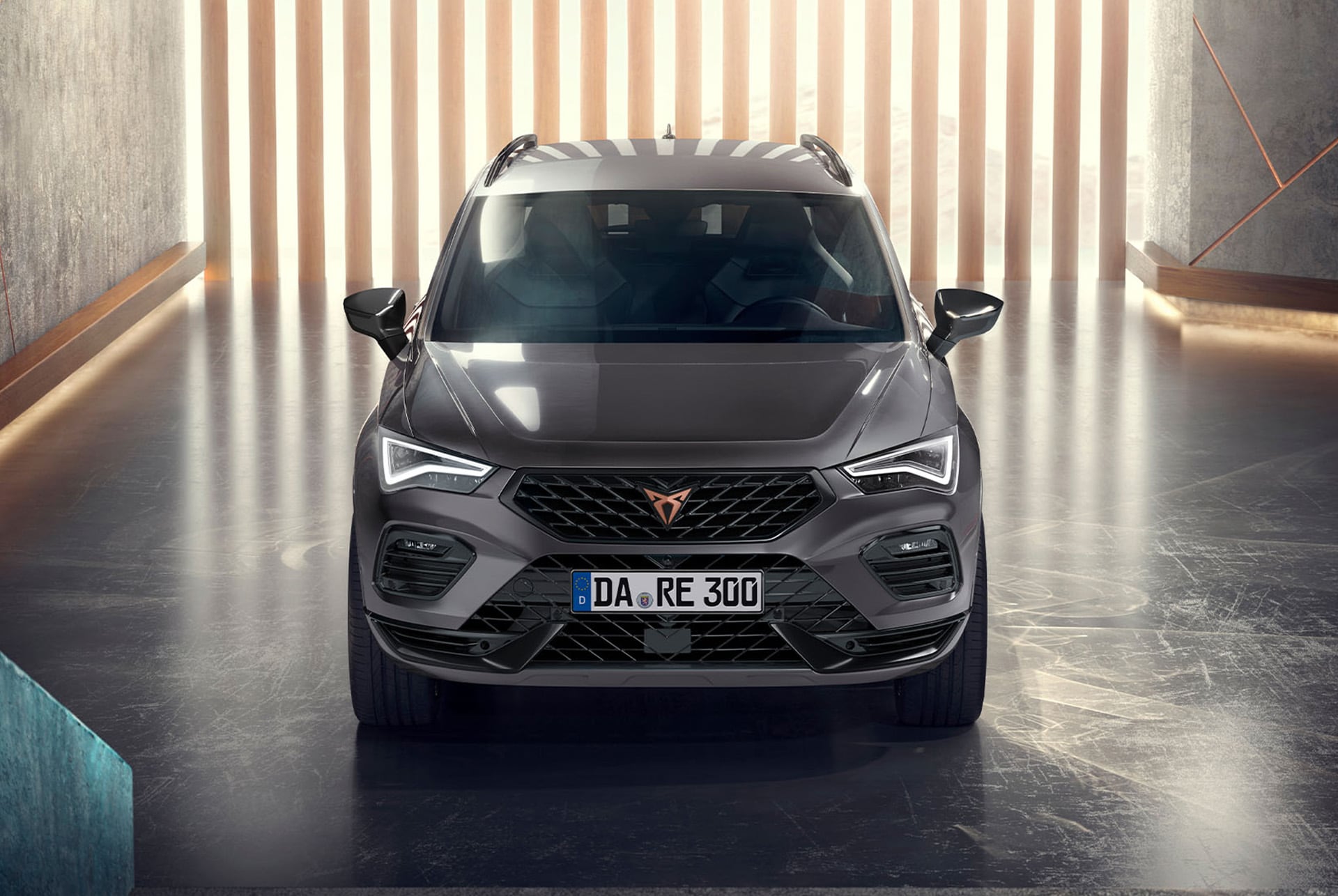 Eine Frontansicht des CUPRA Ateca, eines grauen SUVs, in einer modernen, beleuchteten Umgebung. Das Bild hebt die markante Frontpartie, die LED-Scheinwerfer und das elegante Design des Fahrzeugs hervor.