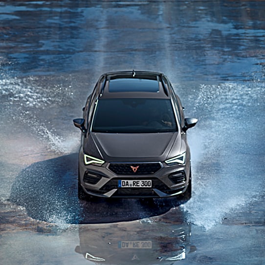 Frontansicht des CUPRA Ateca, der dynamisch durch eine Wasserfläche fährt, wodurch Spritzer um das Fahrzeug entstehen. Das SUV zeigt sein sportliches Design mit markanten LED-Scheinwerfern und einer kraftvollen Präsenz.