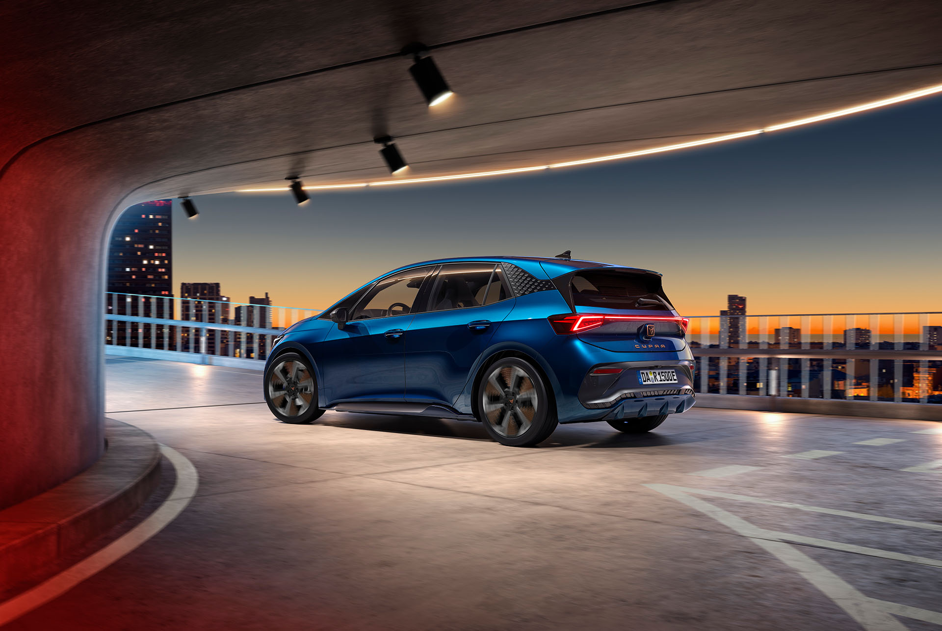Ein blauer CUPRA Born fährt dynamisch durch eine urbane Landschaft bei Sonnenuntergang.