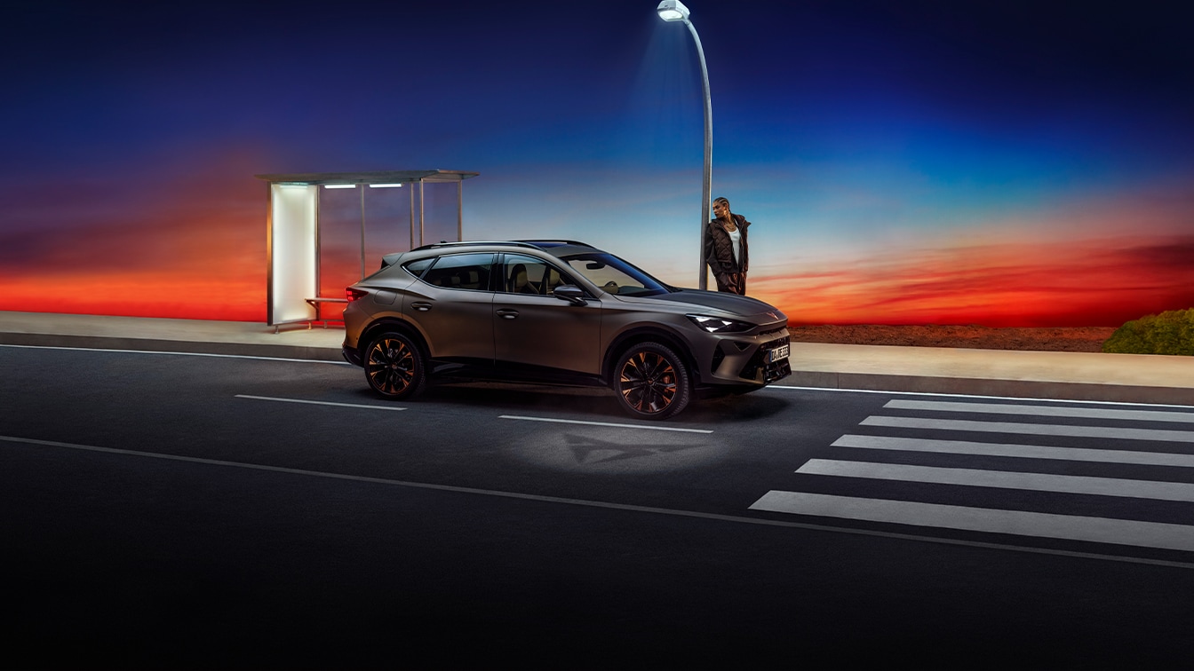 Der CUPRA Formentor bei Sonnenuntergang – sportliches SUV-Coupé vor moderner Kulisse mit markanter Lichtstimmung. Im Hintergrund eine Person an einer Bushaltestelle, die das Fahrzeug betrachtet.“