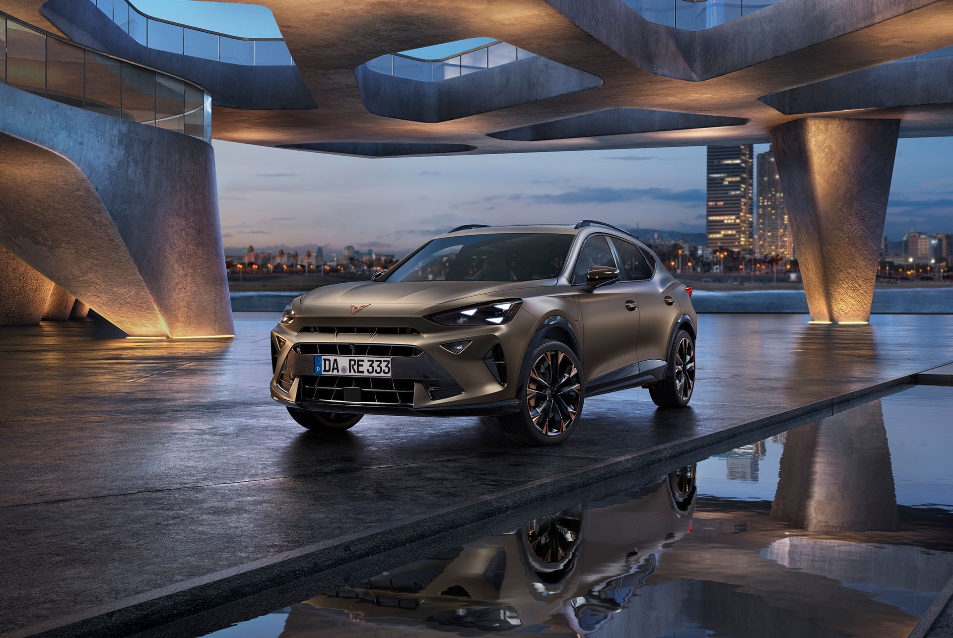 Der CUPRA Formentor in Century Bronze Matt steht auf einer reflektierenden Uferpromenade. Das sportliche und aerodynamische Fahrzeug ist mittig im Bild platziert. Die Kulisse zeigt futuristische Architektur und die leuchtende Skyline von Barcelona in der Abenddämmerung.