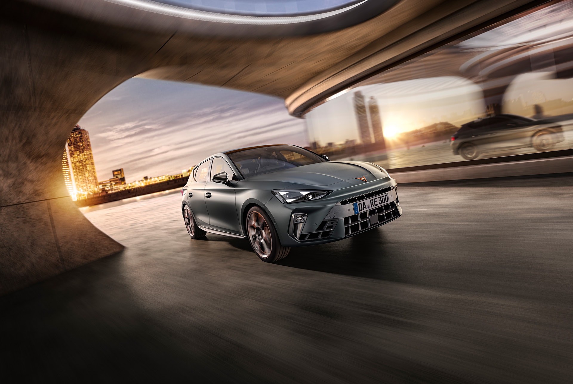 Der CUPRA Leon , in einer Seitenansicht, fährt unter einem Gebäude hindurch. Im Hintergrund ist eine beleutete Skyline in Abendstimmung.