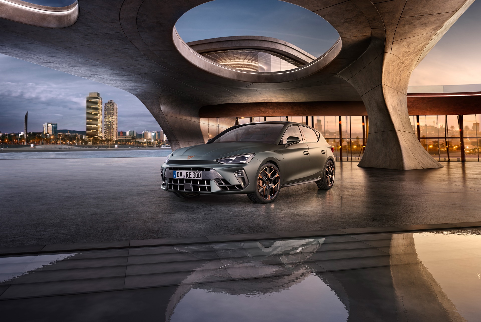 Ein CUPRA Leon 2024 in Enceladus Grau Matt mit Kupfer-Akzent-Leichtmetallrädern, geparkt auf glattem Beton unter einer architektonischen Struktur. Die Skyline von Barcelona im Hintergrund.