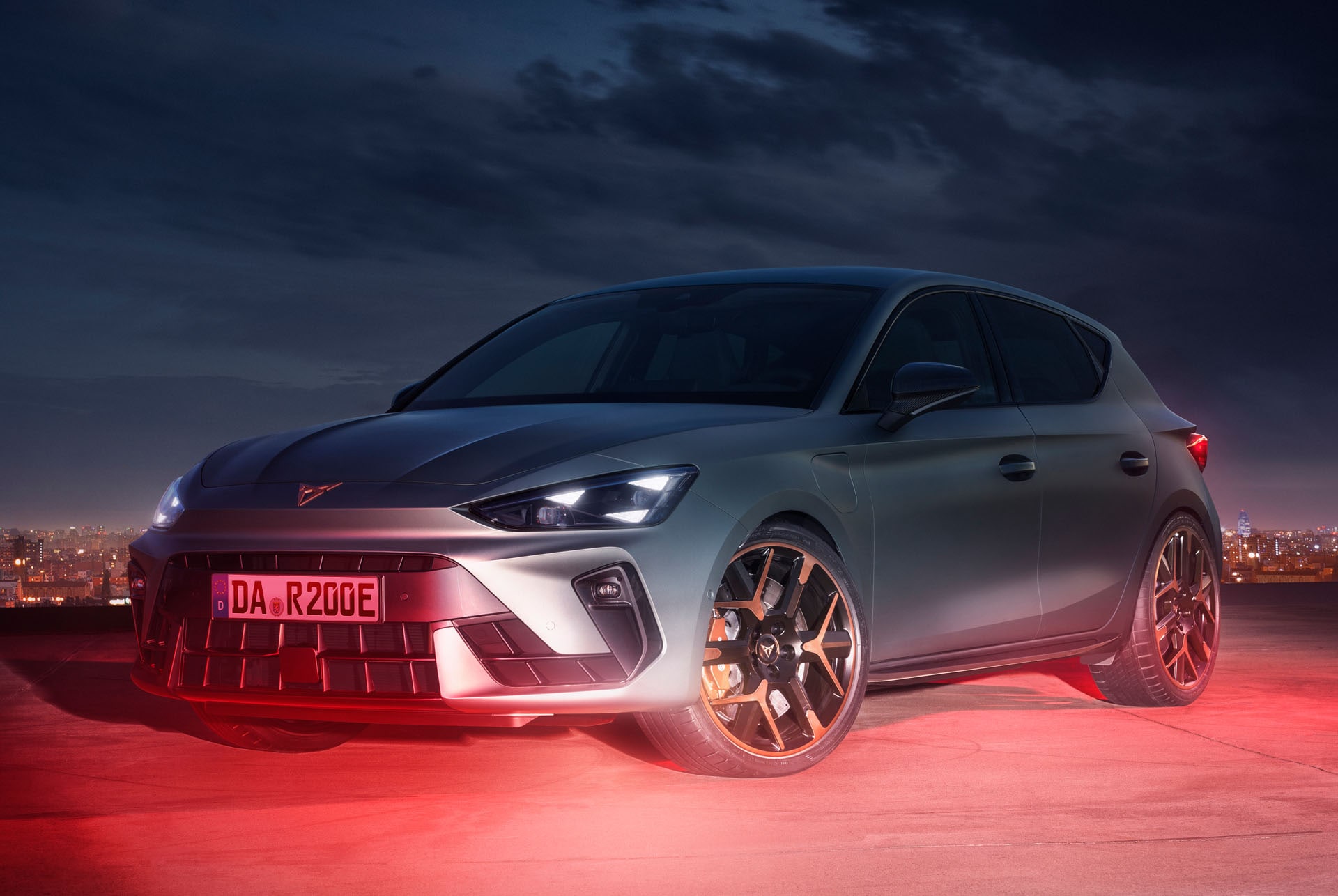 Das Bild zeigt einen CUPRA Leon in einer dynamischen Nachtaufnahme mit einer beleuchteten Stadt im Hintergrund.