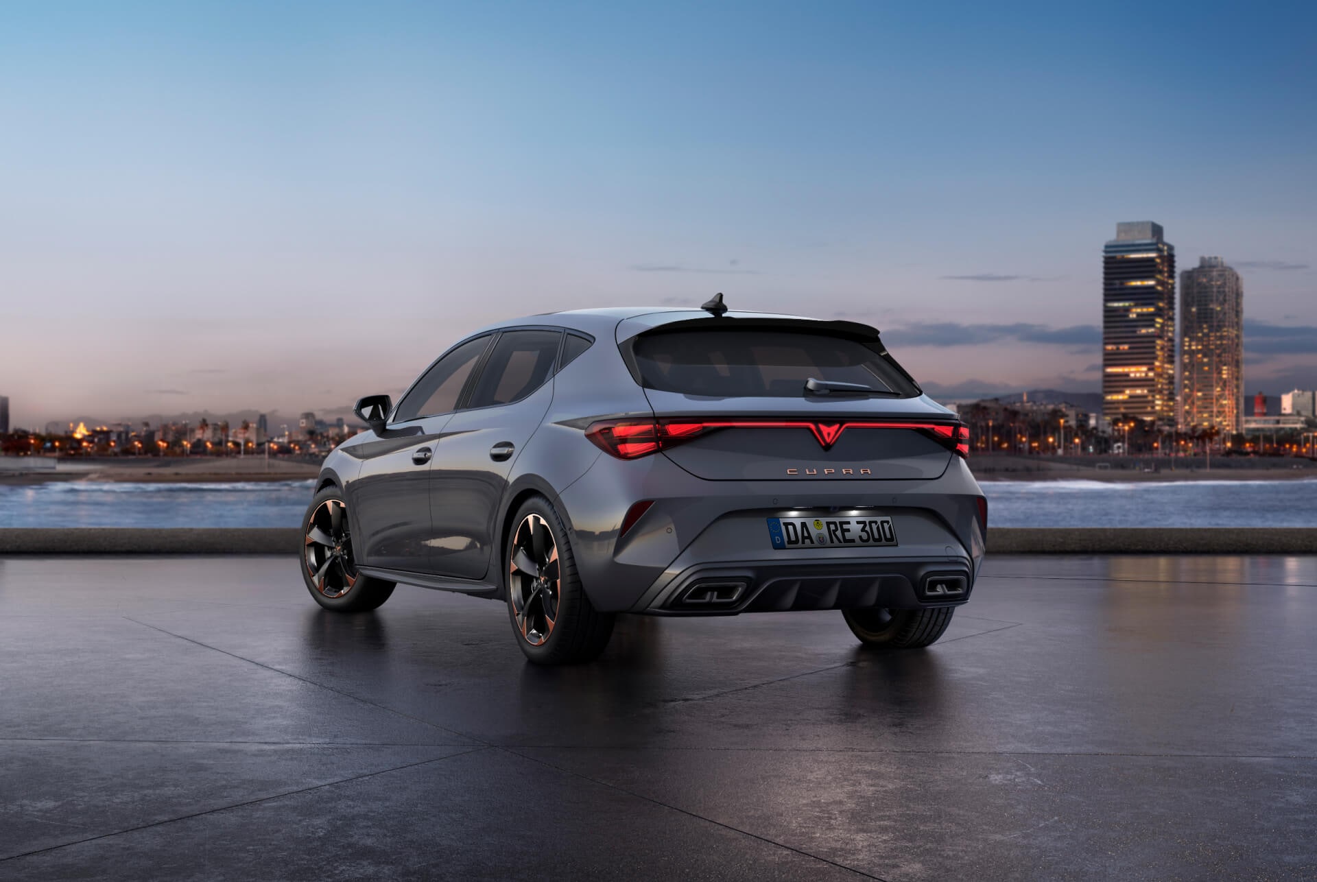 Rückansicht des CUPRA Leon in Glossy Grey mit dynamischer Fahrwerksregelung und schwarzen und kupferfarbenen Leichtmetallrädern. Stadt im Hintergrund bei Sonnenuntergang.