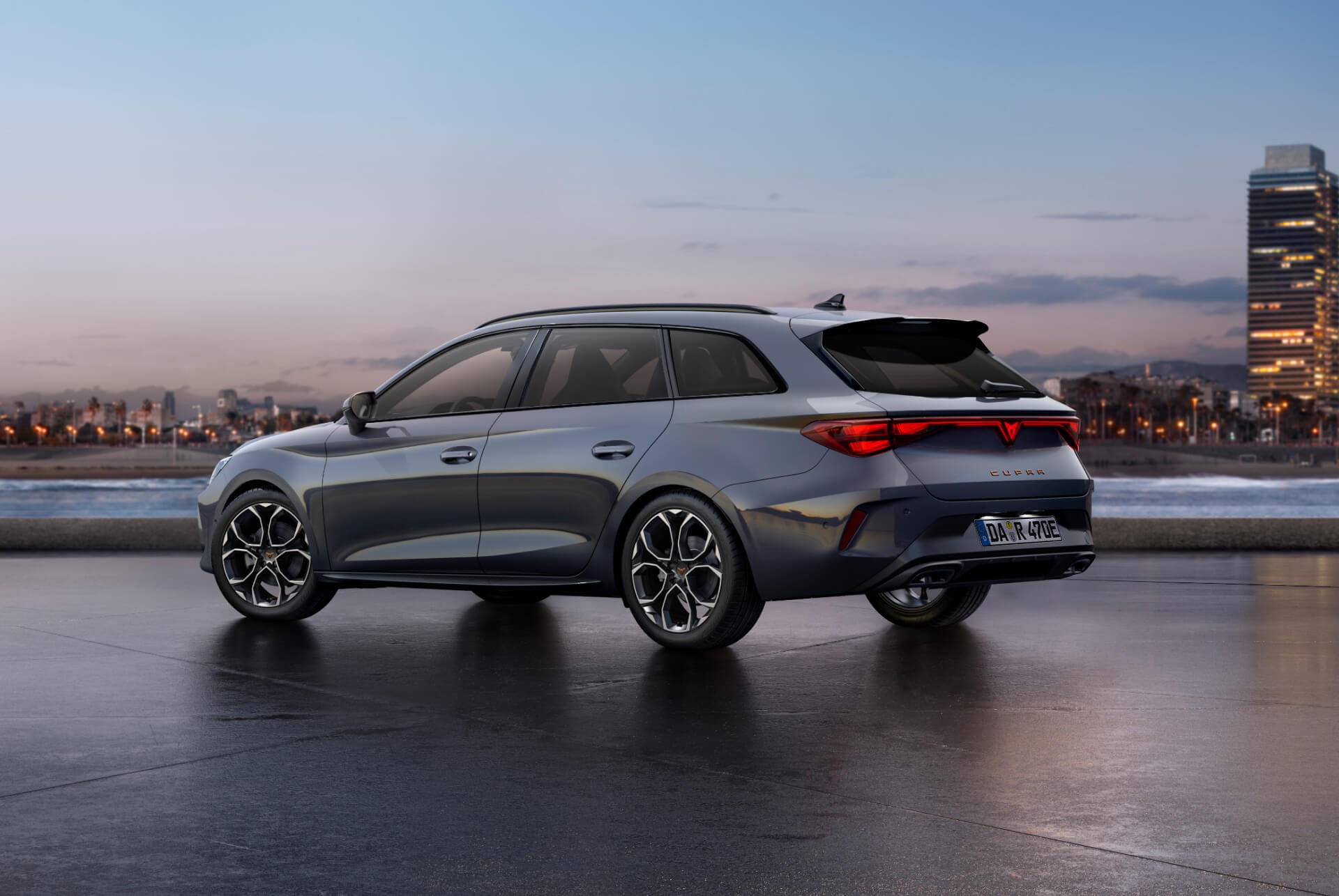 Der sportliche CUPRA Leon Sportstourer, geparkt auf Beton, mit einer beleuchteten Stadtsilhouette in der Dämmerung im Hintergrund. Das Fahrzeug wird in mattem Grau dargestellt.