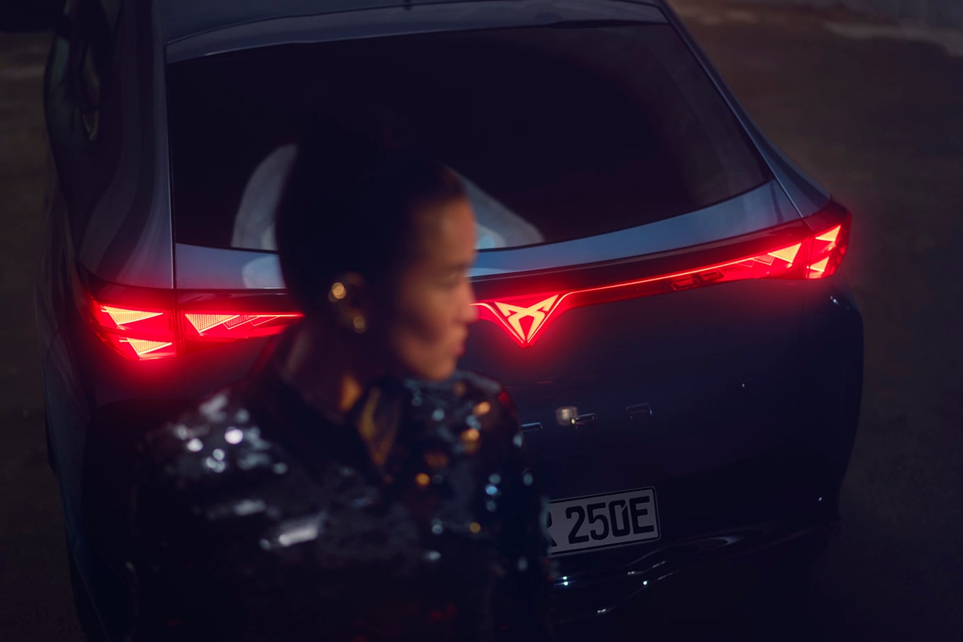 Rückansicht des CUPRA Tavascan mit rot leuchtendem Infinite Light und CUPRA-Logo, das Licht in die Seitenleuchten strahlt.