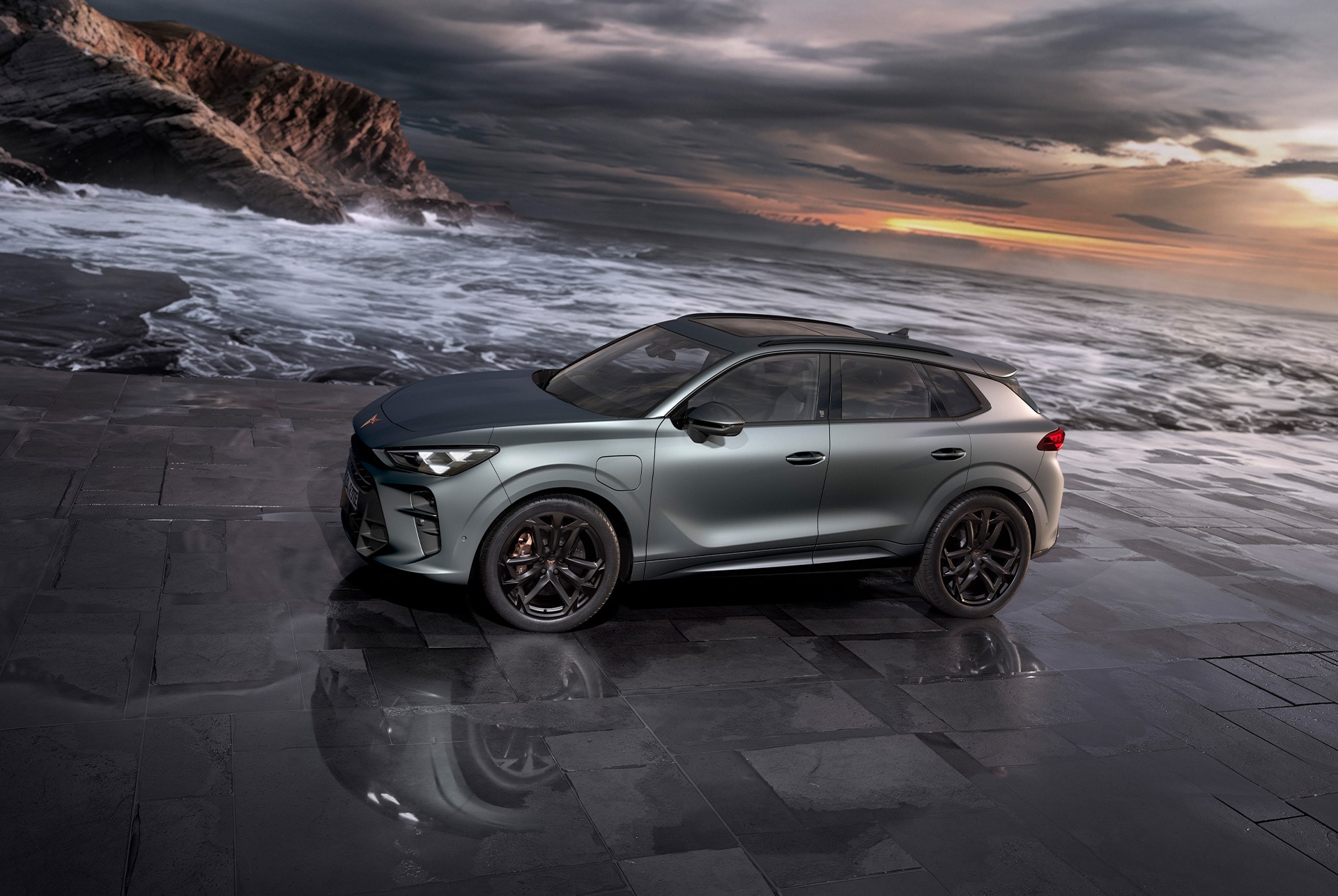 cupra terramar hybrid suv, modell 2024, seitenansicht, mit 20-zoll-leichtmetallfelgen von america's cup und akebono-bremsen, enceladusgrau matt, auf nassem pflaster am meer bei sonnenuntergang.