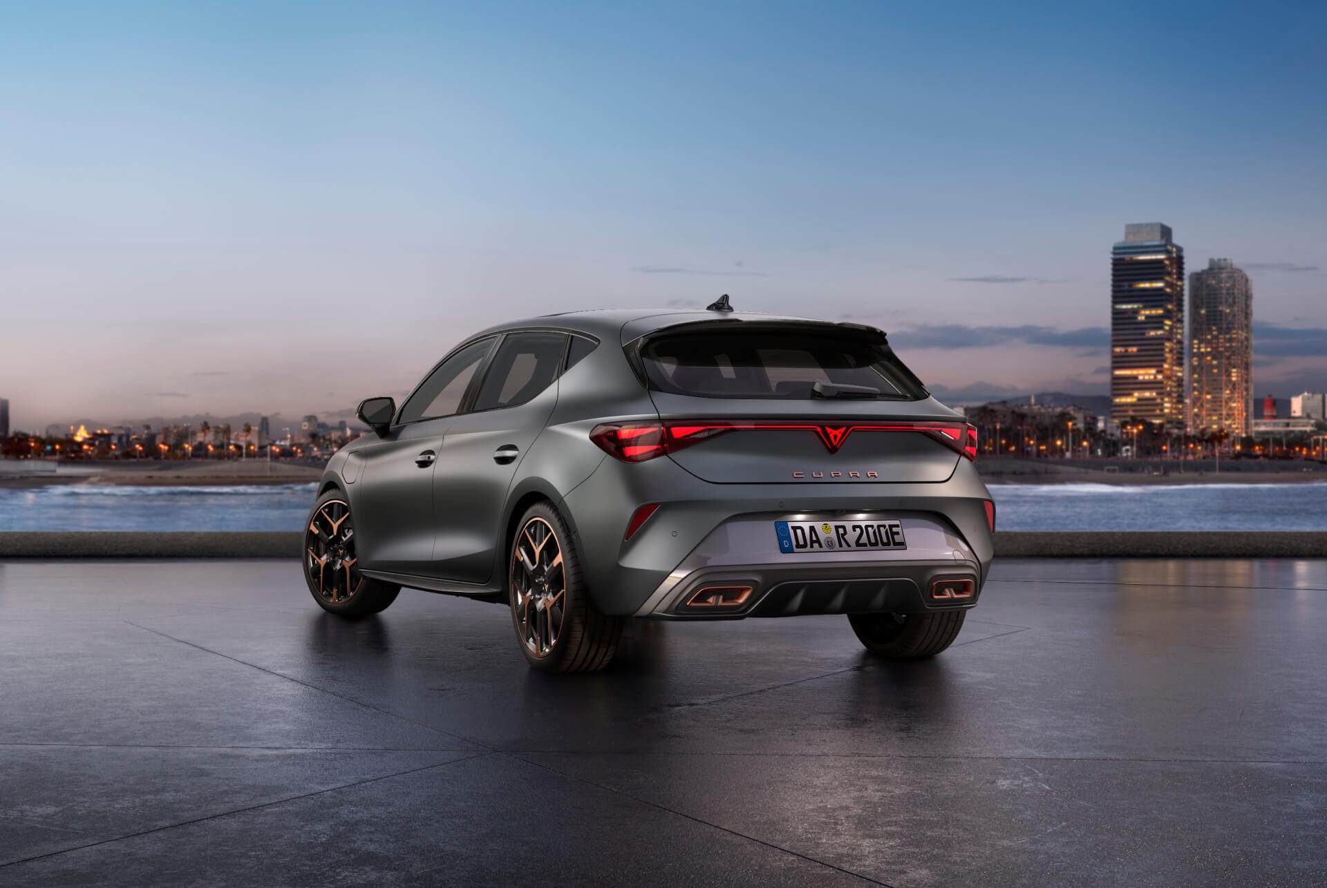 Rückansicht des CUPRA Leon mit dynamischer Fahrwerksregelung und schwarzen und kupferfarbenen Leichtmetallrädern. Stadt im Hintergrund bei Sonnenuntergang.