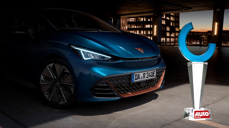 Der elektrische CUPRA Born, Gewinner der Auto Trophy Elektro 2025 in der Kategorie Elektro-Kleinwagen, neben der Importsieger-Trophäe und einer stilisierten Person im Hintergrund.