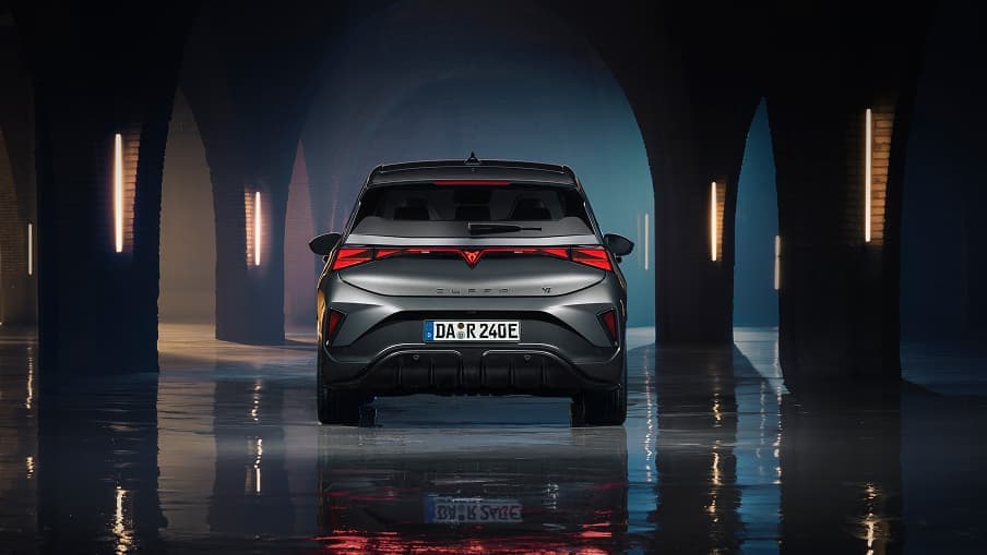CUPRA Born VZ in Timanfaya Grau – Heckansicht in industrieller Gewölbehalle mit Steinbögen und vertikaler Neonbeleuchtung. Das durchgängige LED-Rücklichtband, das CUPRA Logo und die Spiegelung auf nassem Betonboden sind zu sehen.