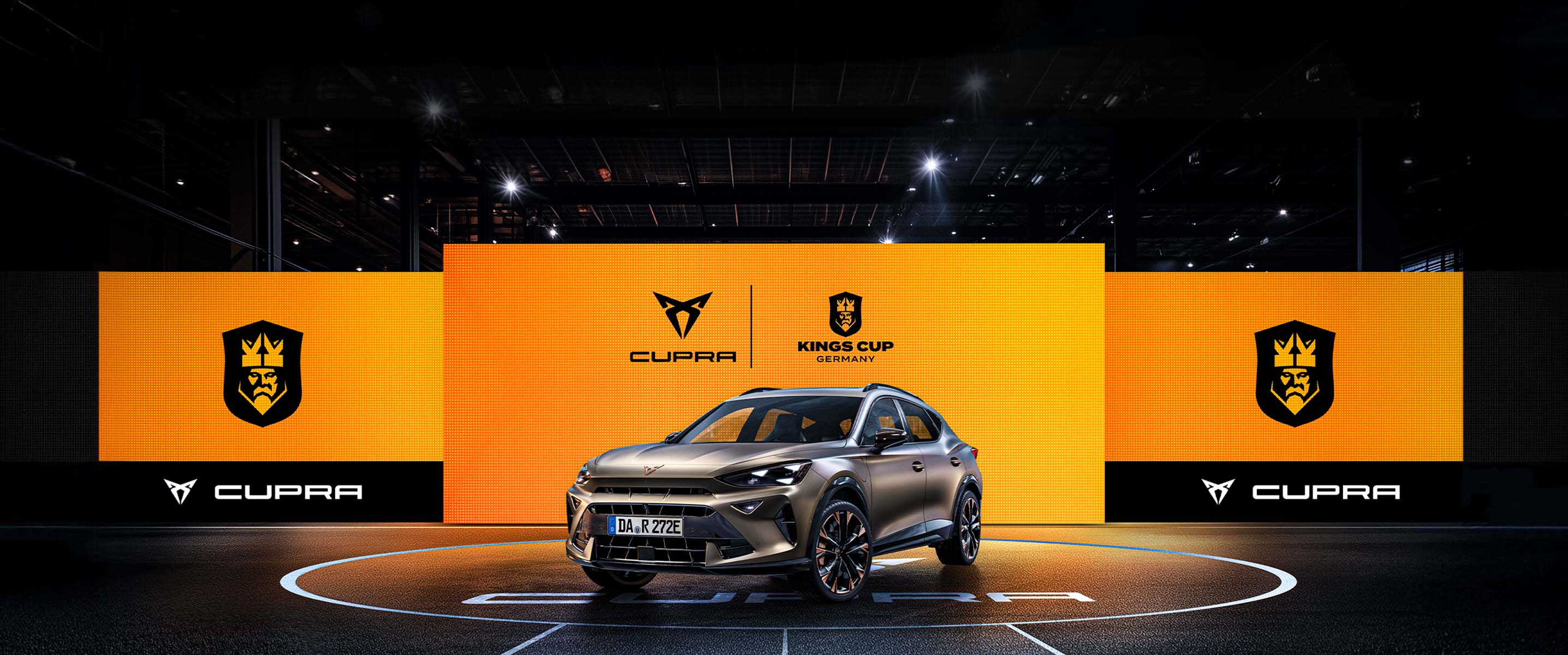 CUPRA Formentor e-HYBRID vor einer Wand aus Screens mit dem CUPRA Logo und dem Kings League Germany Logo. Der CUPRA Formentor e-HYBRID steht im Mittelkreis eines Spielfelds der Kings League.
