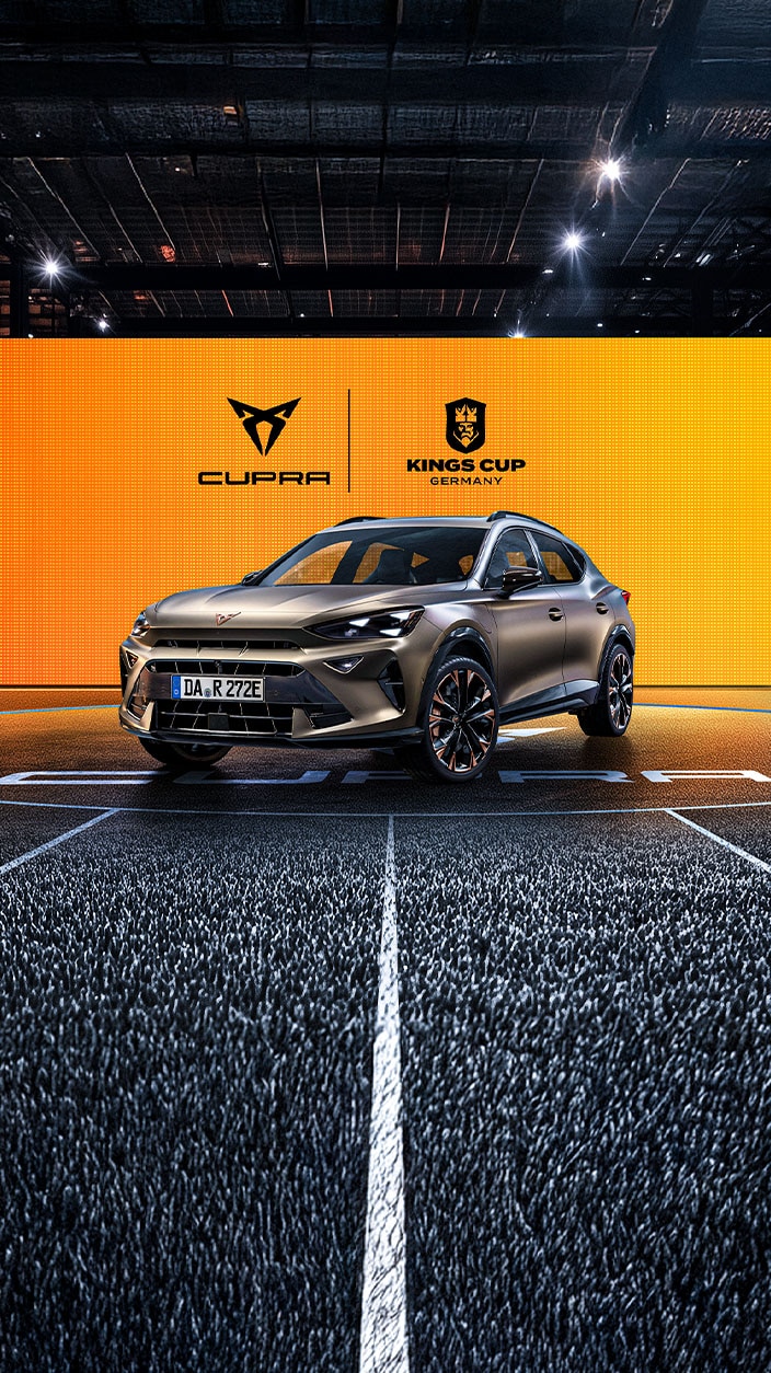 Eine Frau im hellblauem Jumpsuit schwebt auf einer Straße. Sie hält die Hände vor sich ausgestreckt, so als würde sie in einem Fahrzeug sitzen. 