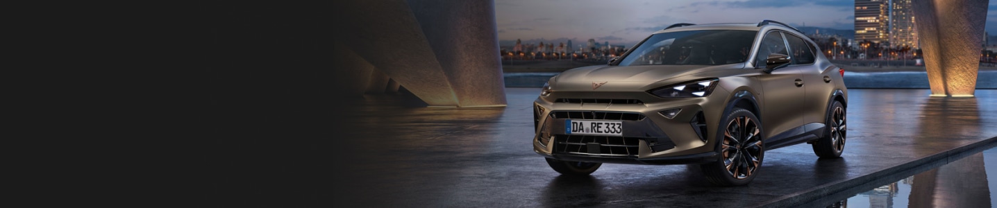 CUPRA Formentor e-HYBRID steht auf einer Asphaltfläche und spiegelt sich im Wasser auf dem Boden. Im Hintergrund ist eine beleuchtete Skyline zu sehen.