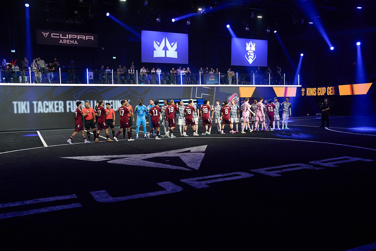 Kings League Bühne mit zwei Teams in Formation, sowie Schiedsrichtern und Linienrichtern.