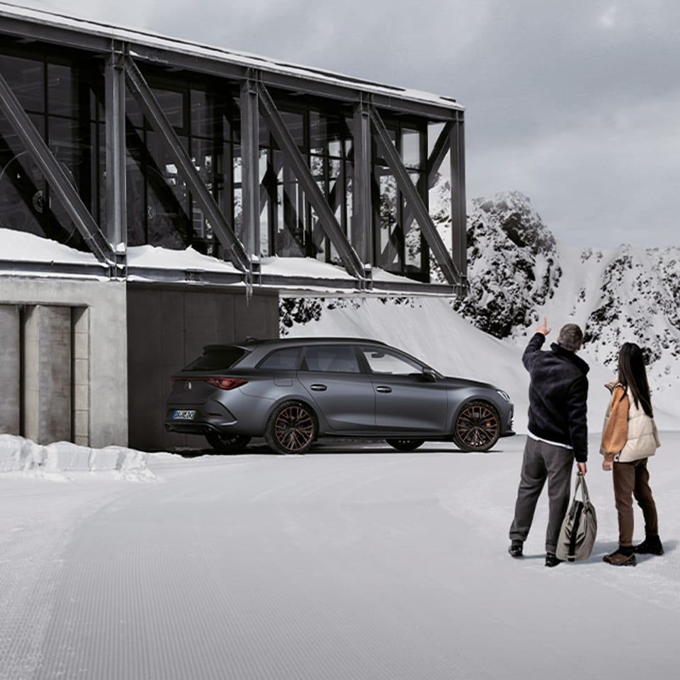 Seitenansicht des neuen CUPRA Leon Sportstourer in einer verschneiten Landschaft vor modernem Gebäude.