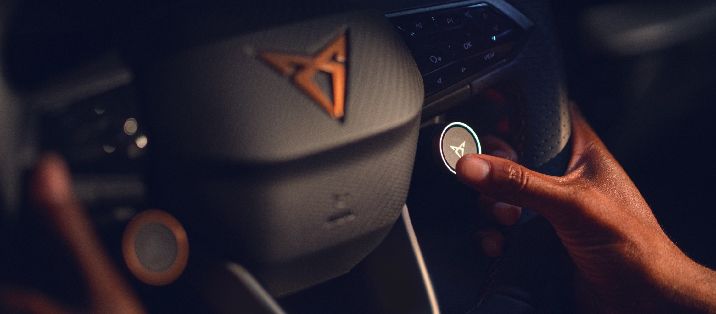 CUPRA-Lenkrad mit Satellitentasten und kupferfarbenem CUPRA-Logo, Nahaufnahme im Innenraum eines Firmenwagens.