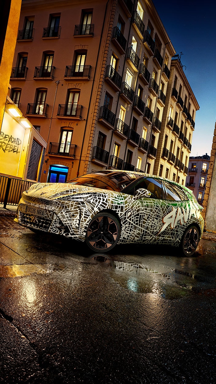 Ein Erlkönig des neuen CUPRA Raval steht vor einer urbanen Stadtkulisse. 