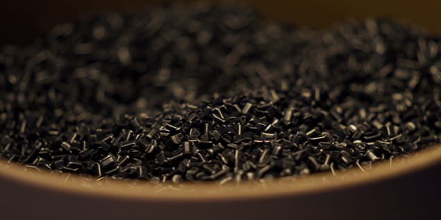 Das Bild zeigt eine Nahaufnahme von kleinen schwarzen Kunststoffpellets oder -granulaten, die häufig als Rohmaterial in der Kunststoffherstellung und beim Spritzgießen verwendet werden.