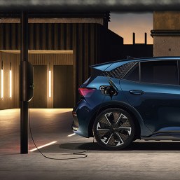 Elektroauto CUPRA Leon beim Aufladen im Parkhaus mit Wandladegerät, Umgebungsbeleuchtung, Beton und Himmel